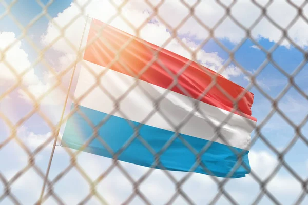 A steel mesh against the background of a blue sky and a flagpole with the flag of luxembourg