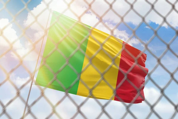 A steel mesh against the background of a blue sky and a flagpole with the flag of mali