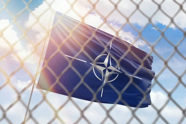 A steel mesh against the background of a blue sky and a flagpole with the flag of nato