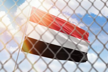 A steel mesh against the background of a blue sky and a flagpole with the flag of yemen