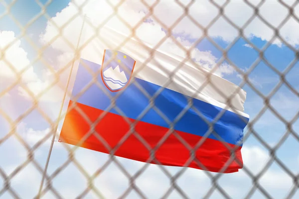 A steel mesh against the background of a blue sky and a flagpole with the flag of slovenia