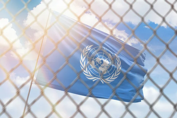 A steel mesh against the background of a blue sky and a flagpole with the flag of united nations