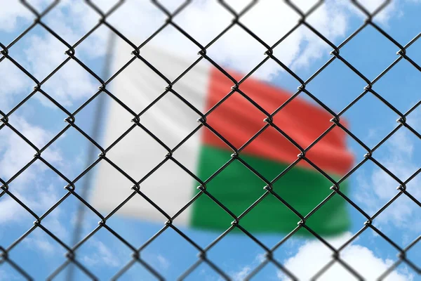 A steel mesh against the background of a blue sky and a flagpole with the flag of madagascar