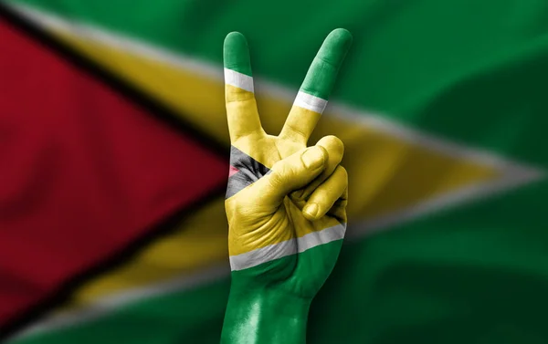 Hand making the V victory sign with flag of guyana