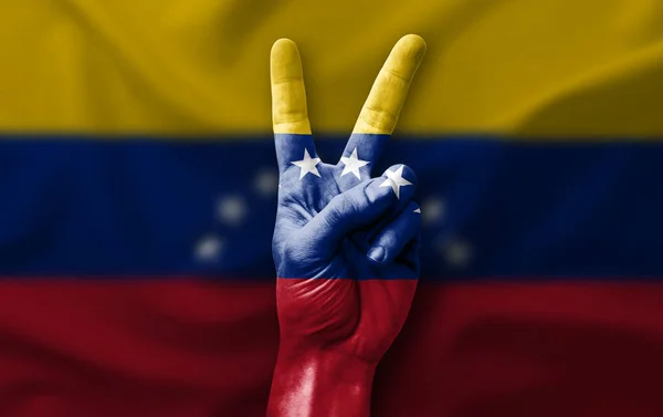 Hand making the V victory sign with flag of venezuela