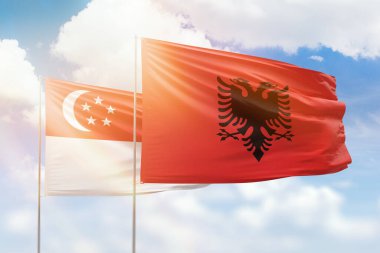 Sunny blue sky and flags of albania and singapore