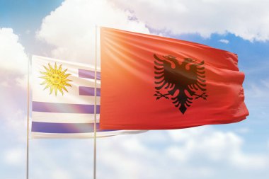 Sunny blue sky and flags of albania and uruguay