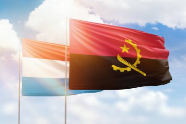 Sunny blue sky and flags of angola and luxembourg