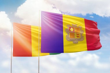 Sunny blue sky and flags of andorra and guinea