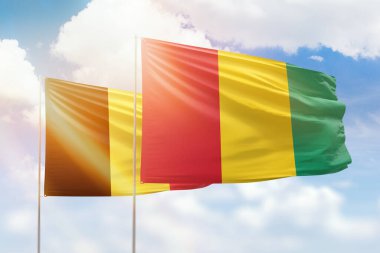 Sunny blue sky and flags of guinea and belgium