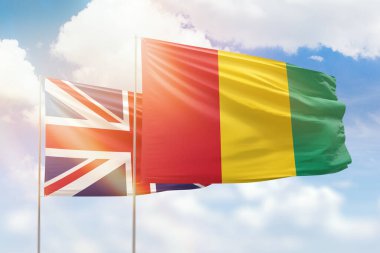 Sunny blue sky and flags of guinea and united kingdom