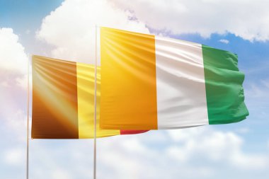 Sunny blue sky and flags of ivory coast and belgium
