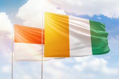 Sunny blue sky and flags of ivory coast and indonesia