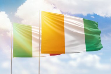 Sunny blue sky and flags of ivory coast and italy