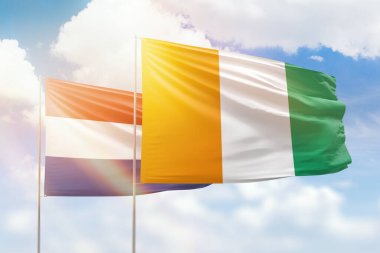 Sunny blue sky and flags of ivory coast and netherlands