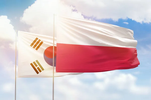 Sunny blue sky and flags of poland and south korea