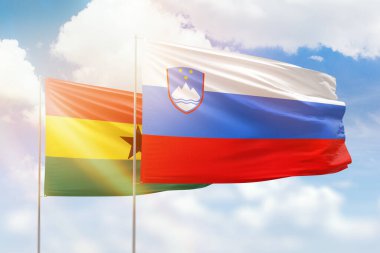 Sunny blue sky and flags of slovenia and ghana