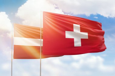 Sunny blue sky and flags of switzerland and latvia
