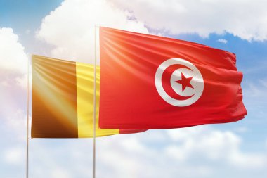 Sunny blue sky and flags of tunisia and belgium