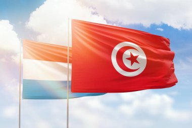 Sunny blue sky and flags of tunisia and luxembourg