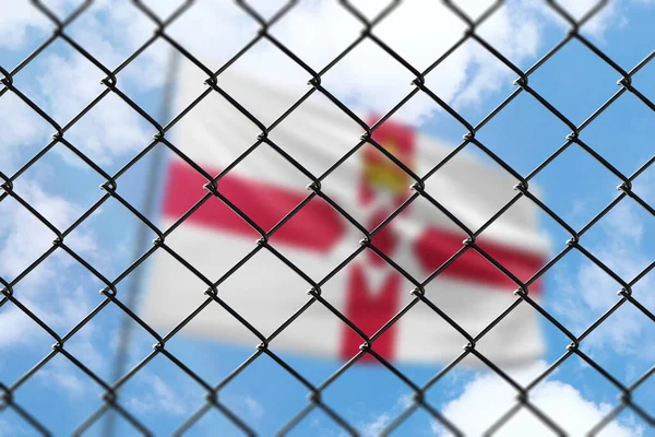 A steel mesh against the background of a blue sky and a flagpole with the flag of northern ireland