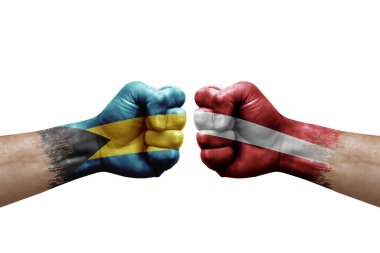 Two hands punch to each others on white background. Country flags painted fists, conflict crisis concept between bahamas and latvia