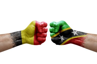 Two hands punch to each others on white background. Country flags painted fists, conflict crisis concept between belgium and saint kitts and nevis