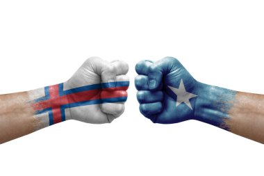 Two hands punch to each others on white background. Country flags painted fists, conflict crisis concept between faroe islands and somalia