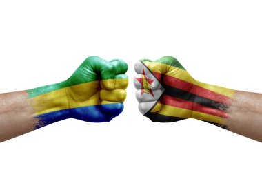 Two hands punch to each others on white background. Country flags painted fists, conflict crisis concept between gabon and zimbabwe
