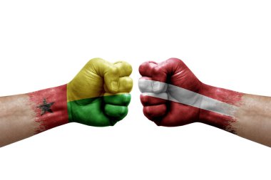 Two hands punch to each others on white background. Country flags painted fists, conflict crisis concept between guinea-bissau and latvia