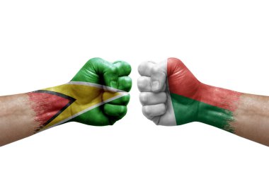 Two hands punch to each others on white background. Country flags painted fists, conflict crisis concept between guyana and madagascar