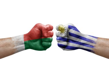 Two hands punch to each others on white background. Country flags painted fists, conflict crisis concept between madagascar and uruguay