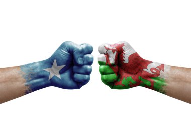 Two hands punch to each others on white background. Country flags painted fists, conflict crisis concept between somalia and wales
