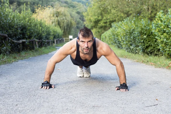 Svalnatý muž dělá push up v parku. — Stock fotografie