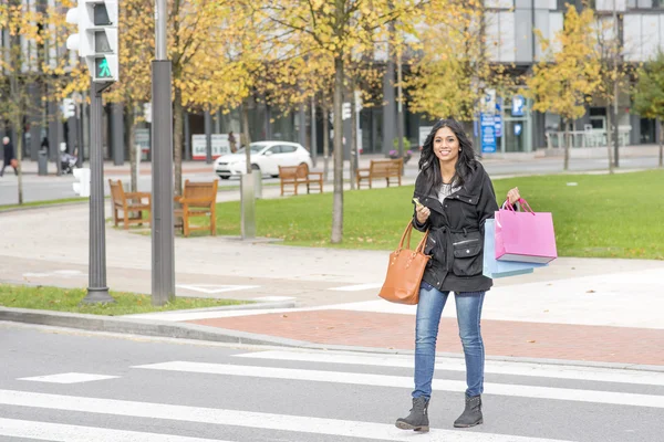 Mulher sorrindo cruzando rua com sacos de compras . — Fotografia de Stock