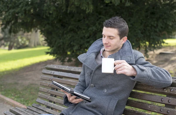 Uomo d'affari seduto su una panca di legno con tavoletta di caffè e computer portatile — Foto Stock