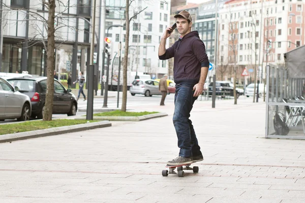 Skateboarder bajando la colina en la calle y hablando por teléfono . —  Fotos de Stock