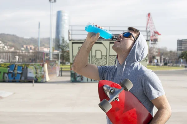 Homem com skate bebendo bebida energética após esporte . — Fotografia de Stock