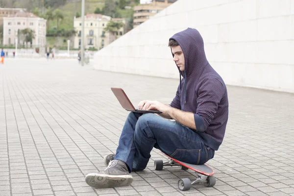 Homem sentado no skate e computador portátil na rua . — Fotografia de Stock