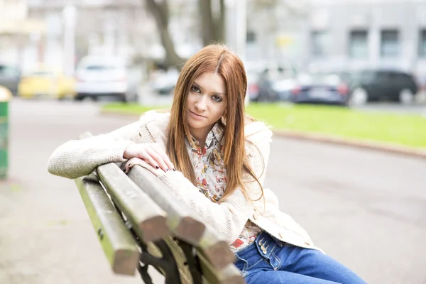 Attraente ragazza seduta su una panchina di legno e guardando la fotocamera . — Foto Stock