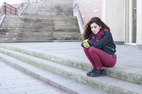 Poważny i zamyślony, młoda dziewczyna, przy użyciu telefonu komórkowego i siedzi na ulicy. — Zdjęcie stockowe