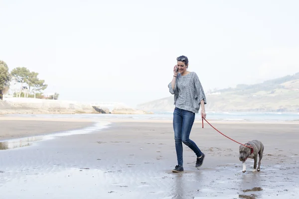 Meisje met hond lopend en pratend op telefoon in het strand. — Stockfoto