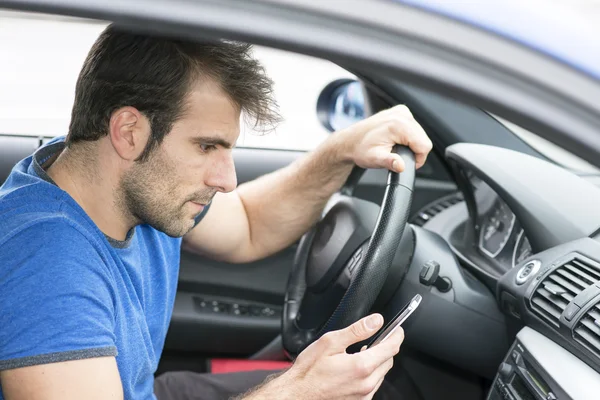男子驾驶，并且在他的智能手机看消息. 图库照片