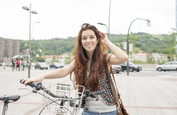 Leende ung kvinna med cykel- och heardphones på gatan. — Stockfoto