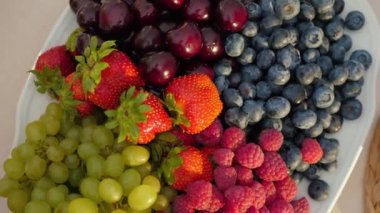 Fresh juicy berries and fruits on plate top view. Rotation of blueberries, strawberries, cherry, grapes, close up
