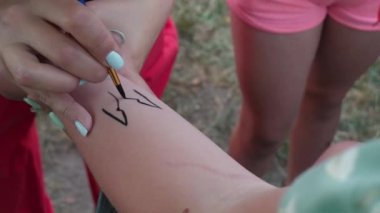Masters hand draws black lines on the girls hand with a brush, a temporary tattoo. An entertainment program for children at a birthday party