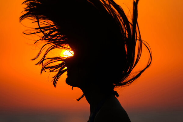 Silhouette of woman tossing hair at sunset