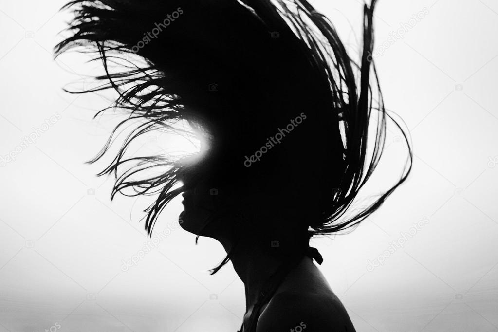 Silhouette of woman tossing hair at sunset black and white