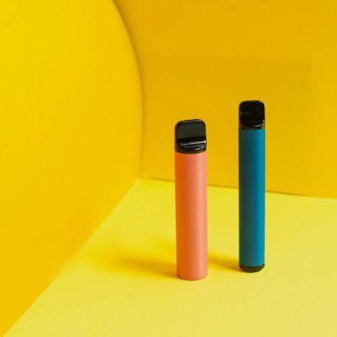 Sarı arka planda gölgeleri olan tek kullanımlık renkli elektronik sigaralar. Modern sigara, buhar ve nikotin konsepti.
