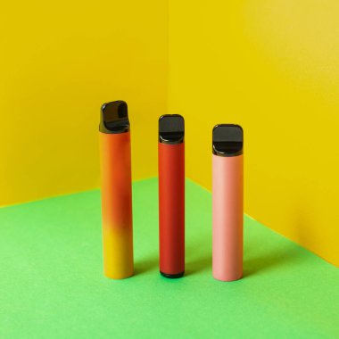 Sarı arka planda gölgeleri olan tek kullanımlık renkli elektronik sigaralar. Modern sigara, buhar ve nikotin konsepti.